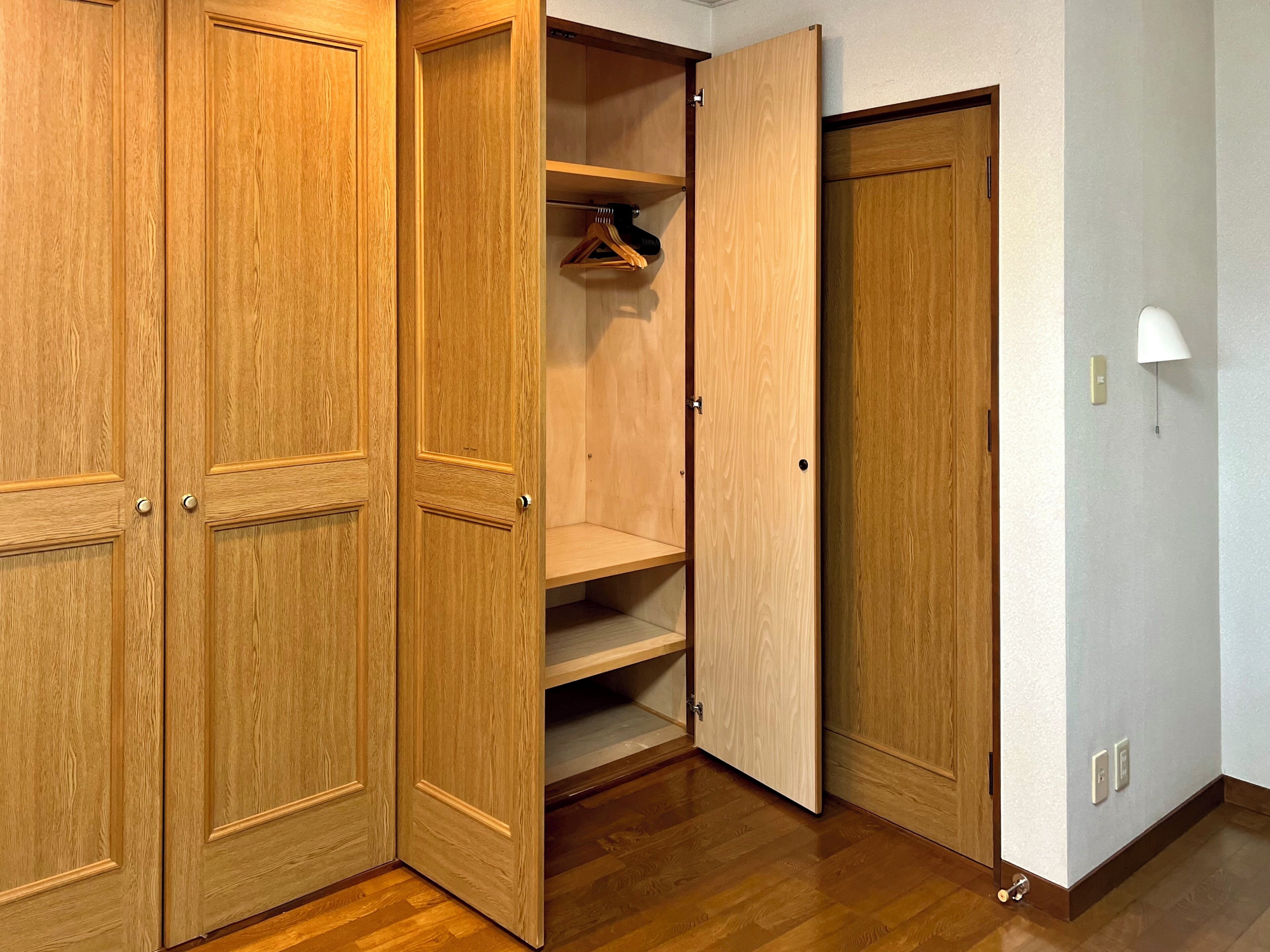 A wooden closet with multiple shelves and hanging space, a white wall lamp, and a door with a handle.