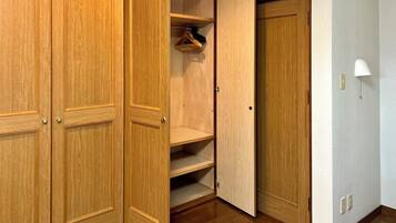 A wooden closet with multiple shelves and hanging space, a white wall lamp, and a door with a handle.