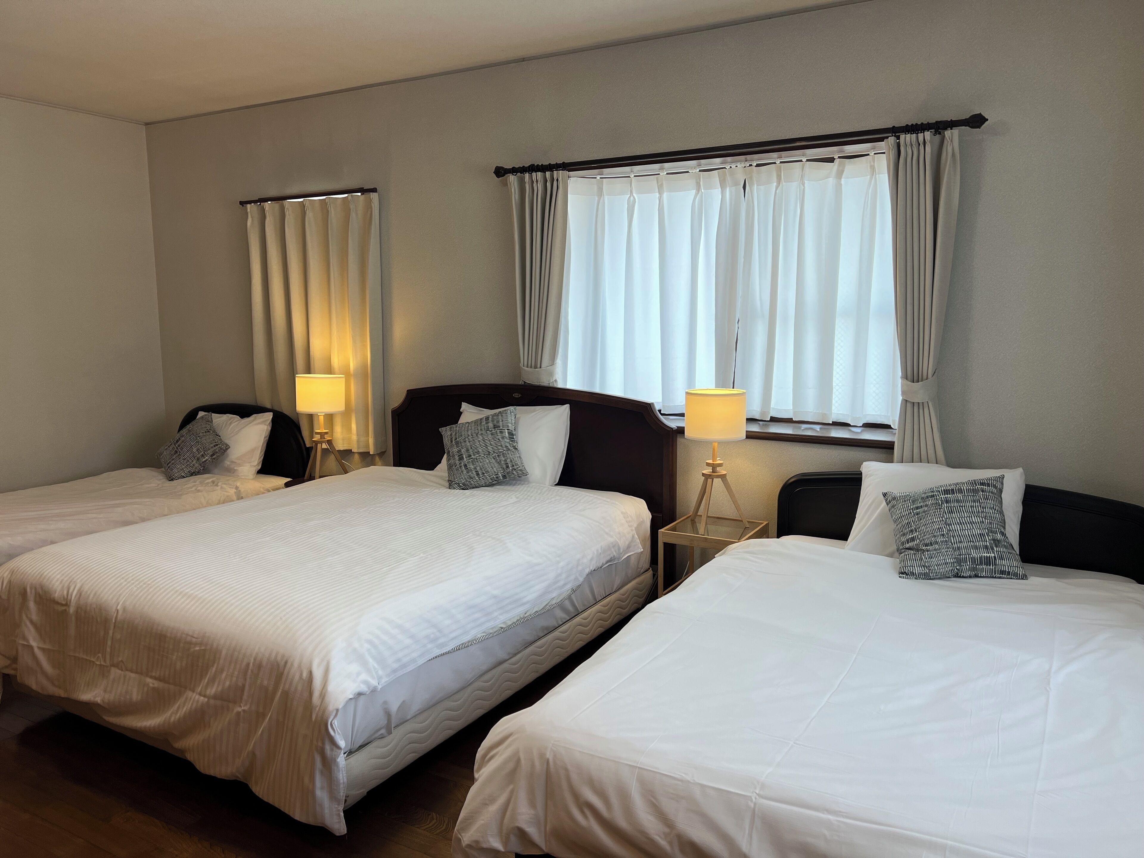 Une chambre d’hôtel avec deux lits simples, une table de chevet avec une lampe et une fenêtre avec des rideaux.