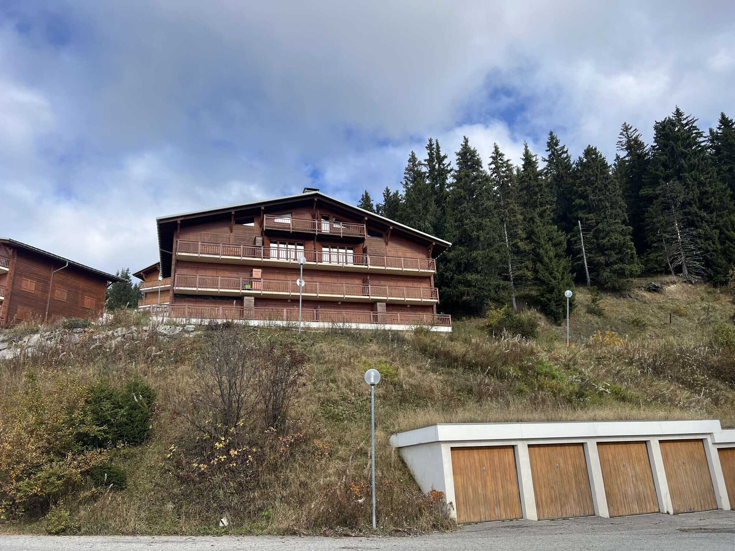 A multi-story wooden building with balconies, situated on a hillside with a forest backdrop.