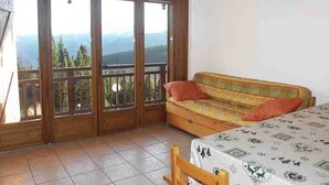 A room with a wooden balcony, a sofa, and a bed with a patterned bedspread. - 3-room apartment, near slopes, Les Saisies, sleeps 8 (Les Saisies)
