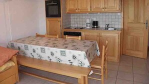 A compact kitchen with wooden cabinets, a microwave, a coffee maker, and a dining table with a patterned tablecloth. - 3-room apartment, near slopes, Les Saisies, sleeps 8 (Les Saisies)