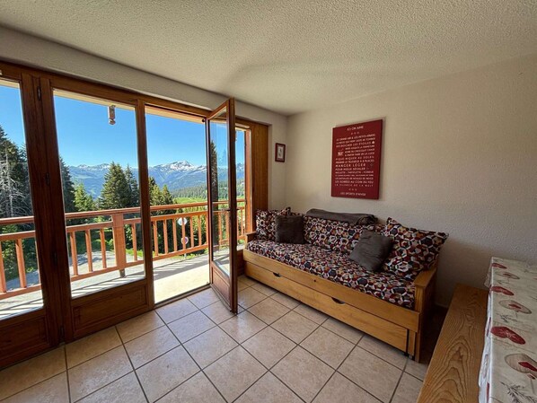 A room with a wooden sofa, a bench, and a view of mountains through large glass doors.