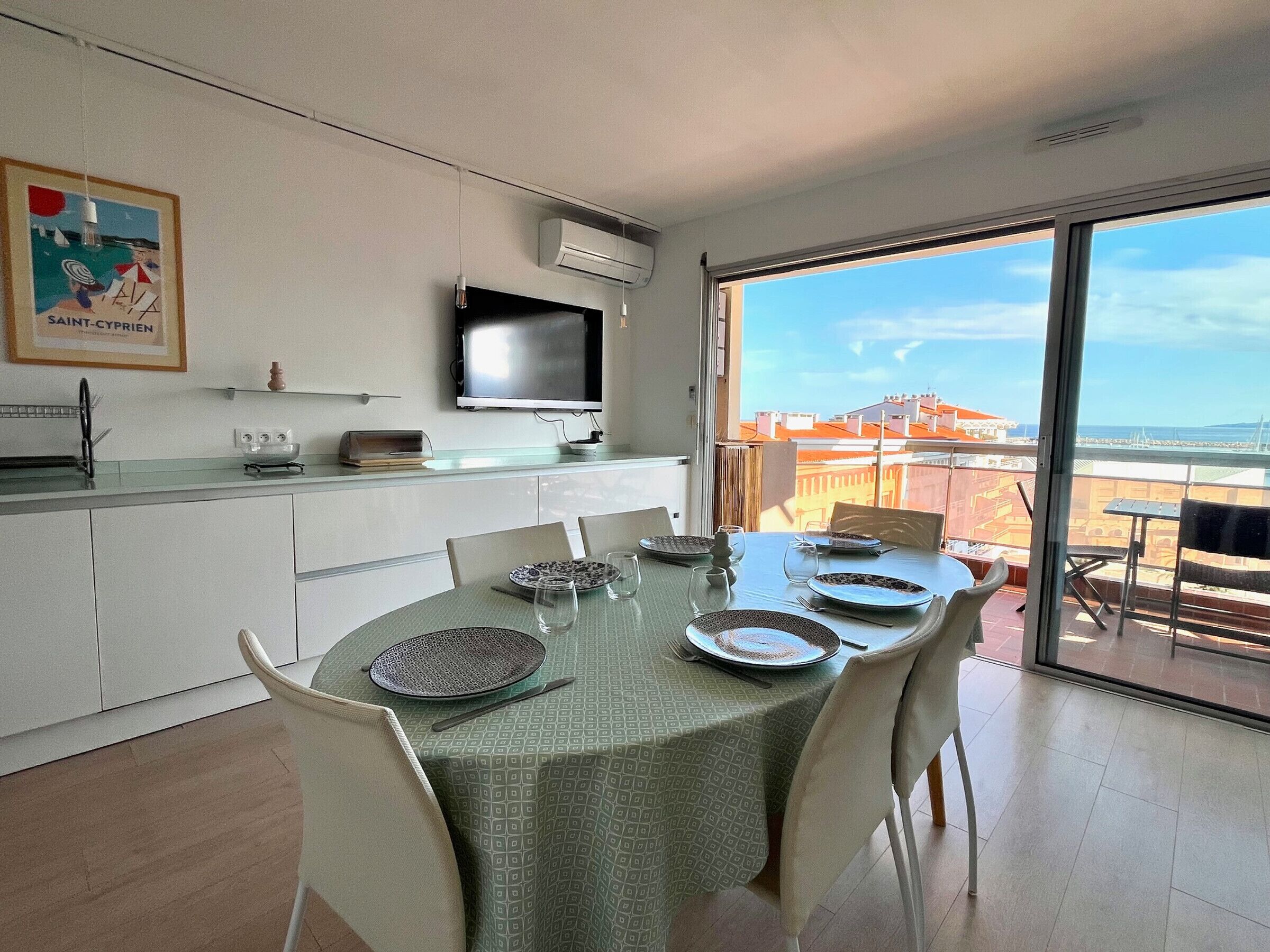 Zona pranzo con tavolo apparecchiato per quattro, cucina con televisore e balcone con vista.