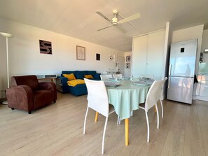Un espacio de estar moderno con comedor, un sofá, un sillón marrón y una cocina con refrigerador.