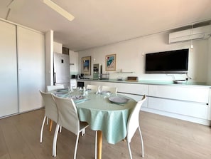 Una cocina moderna con comedor, que incluye una mesa para cuatro personas, armarios blancos y un televisor de pantalla plana sobre la encimera.