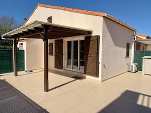 Ein überdachter Patio-Bereich mit einer Pergola, Schiebetüren und einem gefliesten Boden.