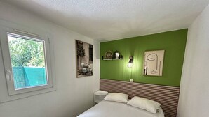 A bedroom with a bed, a window, a wall-mounted light, and a framed picture. - Renovated pavilion in Argelès-sur-Mer, air-conditioned and pool! (Argelès-sur-Mer)