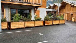 A wooden chalet with a balcony, large windows, and a wooden fence with plants. - Beautiful T3 apartment in new residence with parking and WIFI, near village and ski bus (Samoëns)