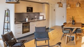 A modern kitchen with white cabinets, a central island, and a dining area with wooden tables and chairs. - Beautiful T3 apartment in new residence with parking and WIFI, near village and ski bus (Samoëns)