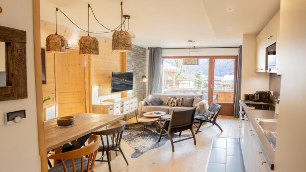 A modern kitchen with a dining area, wooden flooring, and a large window offering a view of the outdoors. - Beautiful T3 apartment in new residence with parking and WIFI, near village and ski bus (Samoëns)