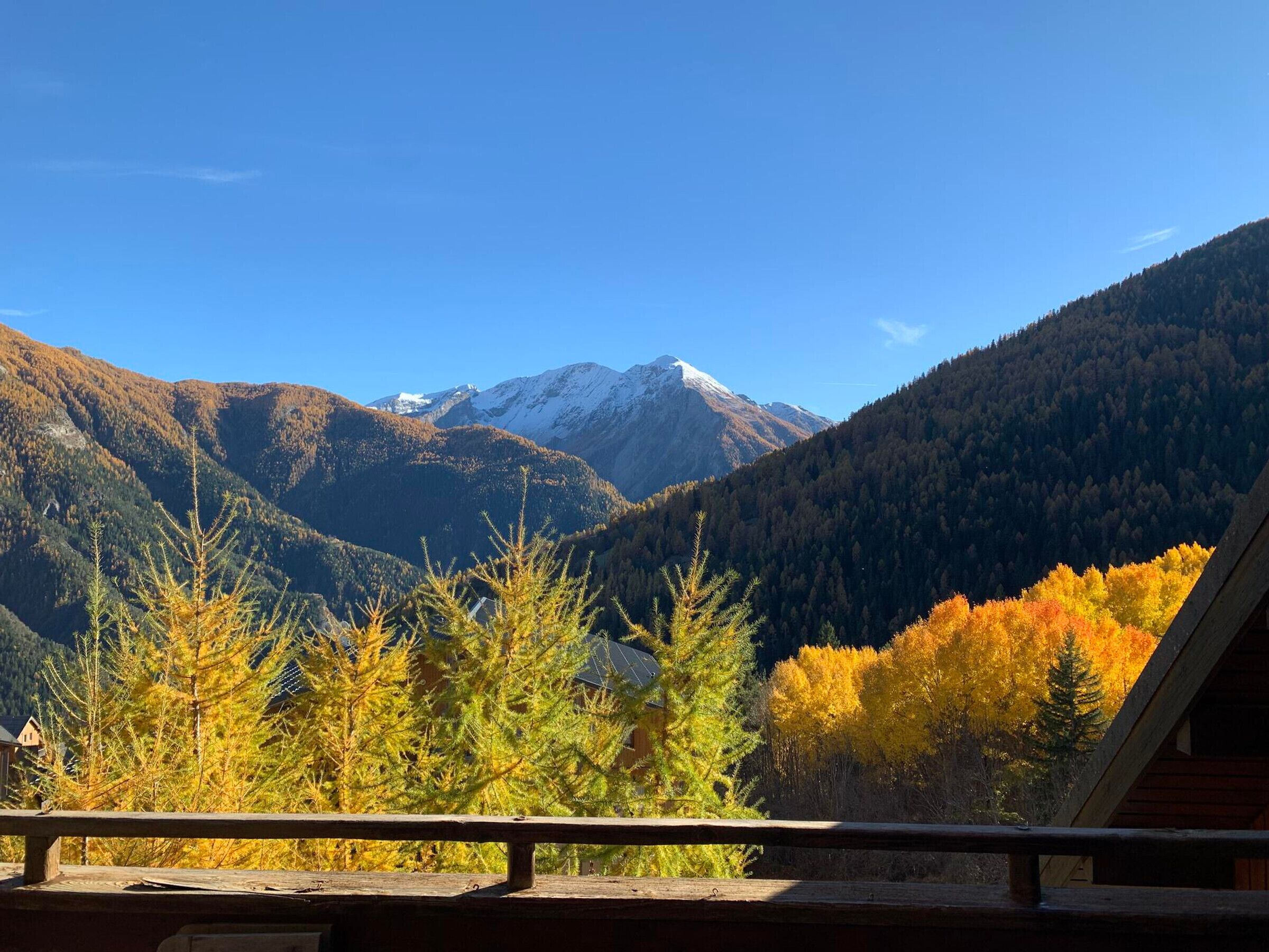 A mountain cabin with a view of snow-capped peaks and autumn foliage.