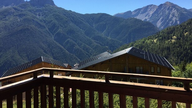 Une cabane en bois dotée de panneaux solaires, entourée de montagnes boisées.