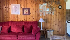 Un salon chaleureux avec un canapé en velours rouge, des murs lambrissés et divers tableaux encadrés représentant des motifs botaniques.
