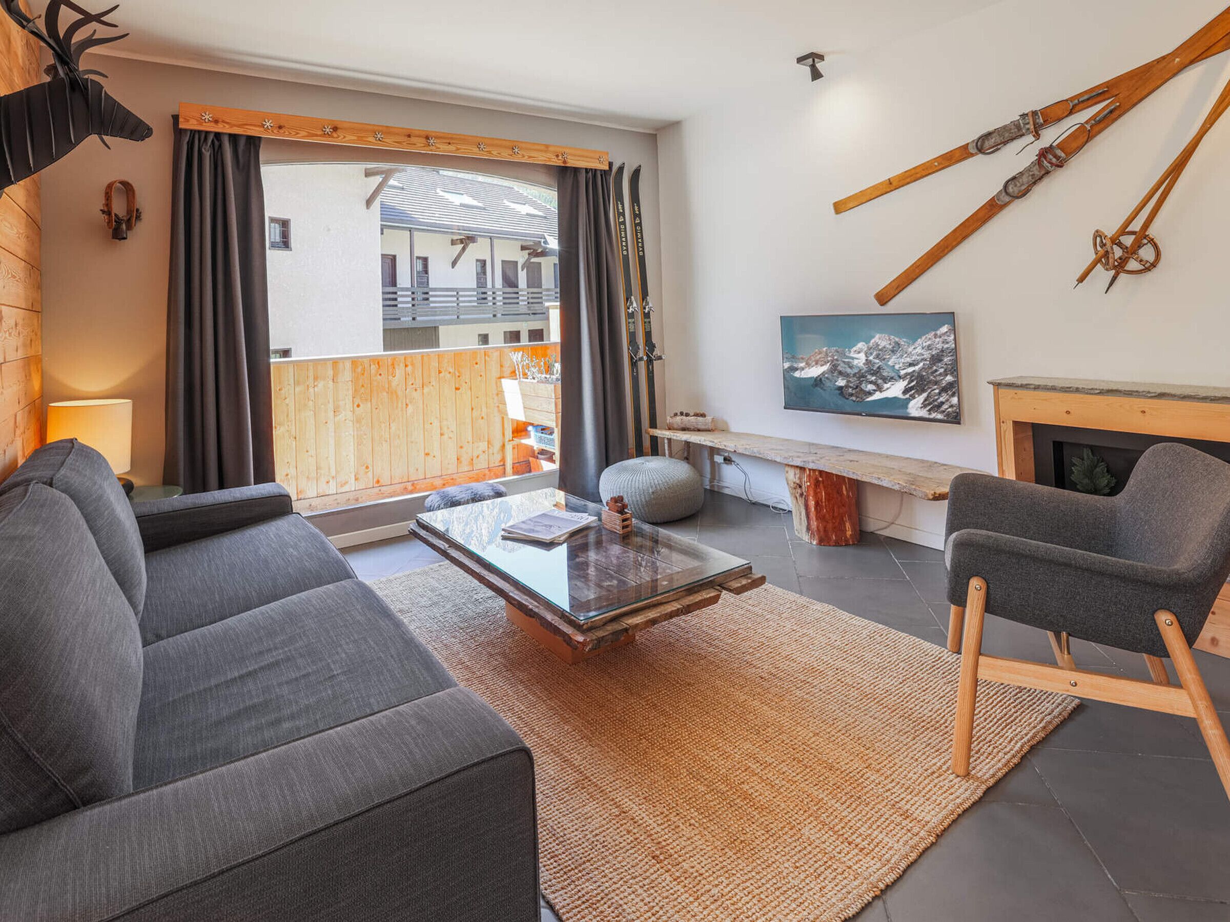 A modern living room with a sofa, a coffee table, and a fireplace. There are skis and a painting on the wall.