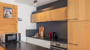 A modern kitchen with wooden cabinets, a black countertop, a microwave, a coffee maker, and a toaster. - Central apartment with sunny terrace (Le Monêtier-les-Bains)