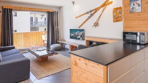 A modern living room with a sofa, coffee table, and a kitchen area with a microwave. - Central apartment with sunny terrace (Le Monêtier-les-Bains)