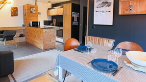 A modern kitchen with wooden cabinets, a dining area with a table set for two, and a cozy seating area with a sofa and chairs. - Central apartment with sunny terrace (Le Monêtier-les-Bains)