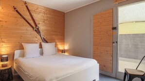 A modern bedroom with a wooden headboard, a large bed with white linens, a nightstand with a lamp, and a view of the outside through a sliding door. - Central apartment with sunny terrace (Le Monêtier-les-Bains)