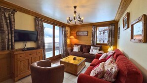 A cozy living room with a television, a sofa, a red armchair, and a wooden cabinet. - Comfortable apt for 6 in Saint-Martin near slopes, parking, WiFi (Saint-Martin-de-Belleville)