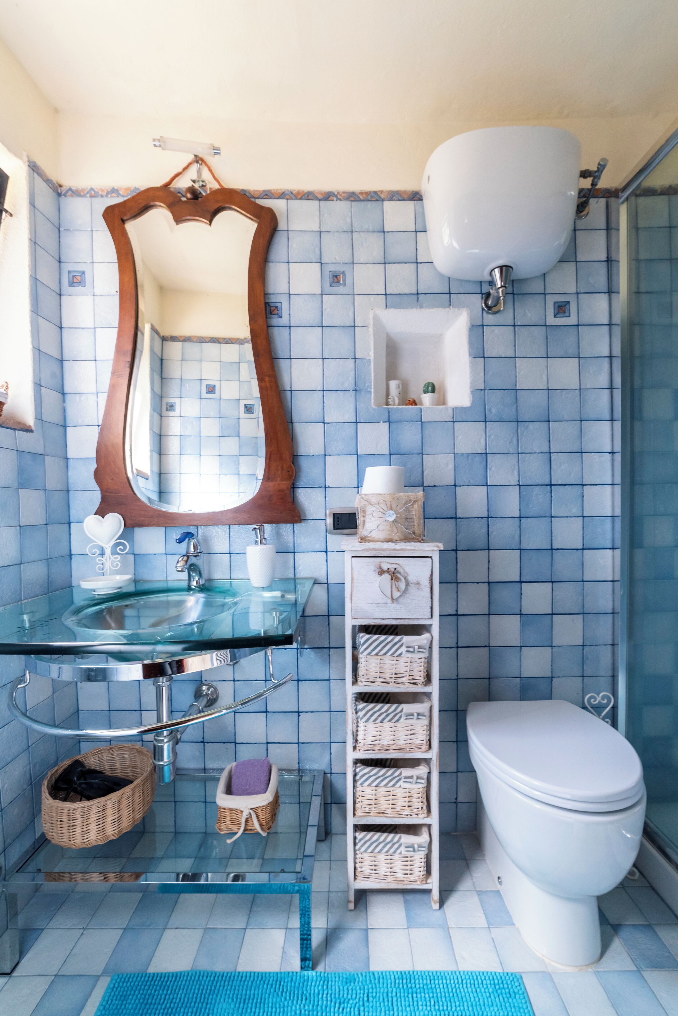 Une salle de bain avec un lavabo en verre, un miroir à cadre en bois, des toilettes blanches et un mur recouvert de carreaux bleus.