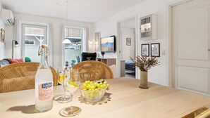 Un coin repas avec une table en bois, des chaises en osier, une bouteille de LORINA, un saladier de fruits et un vase rempli de fleurs séchées.