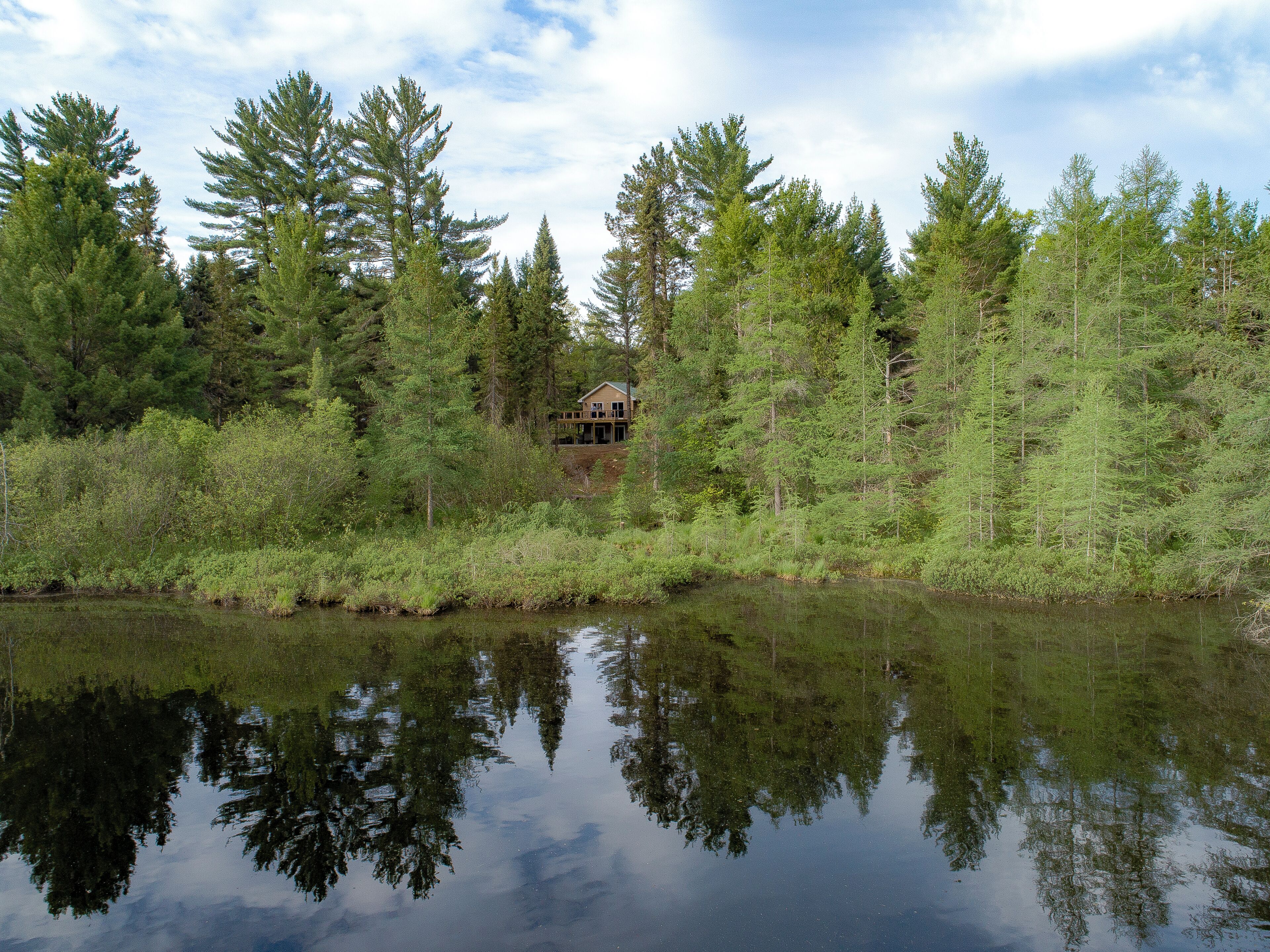 A house surrounded by dense forest and a calm lake.