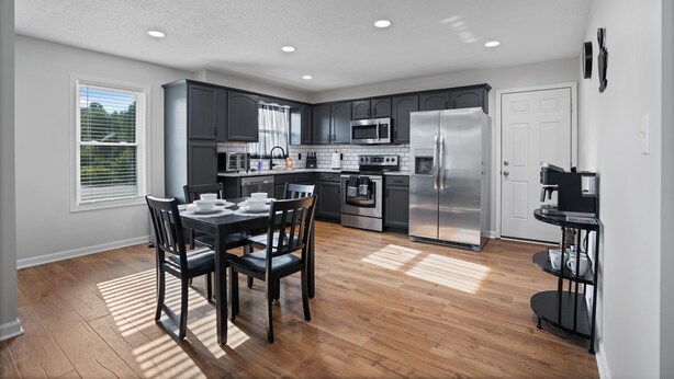 Una cocina moderna con armarios oscuros, electrodomésticos de acero inoxidable y un comedor con mesa y sillas de madera.