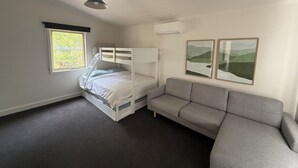 A bedroom with a bunk bed, a grey sofa, a window with a view of greenery, and two framed pictures on the wall. - 'Pippa's Place'
Family friendly, newly renovated sanctuary atop Mt Little Joe (Warburton)