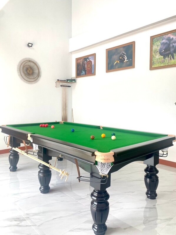 A pool table with balls, a clock, and framed pictures on the wall.