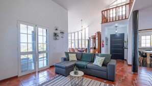 A spacious living room with a large sofa, a coffee table, and a view of the outdoors through large windows. - Casa Almada (Ribeira Brava)