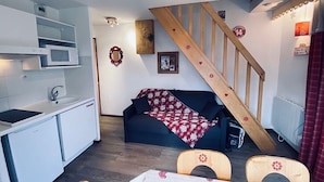 A compact living space with a kitchenette, a sofa with a red and white patterned blanket, a wooden staircase, and a small table with two chairs. - Praz de Lys resort, duplex apartment 200 metres from the ski lifts (Taninges)