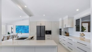 Cocina moderna con una isla central, armarios blancos, electrodomésticos de acero inoxidable y un amplio ventanal con vistas.