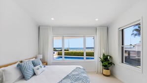 Un dormitorio con una cama grande, vista a la piscina y al océano, y una planta en maceta.