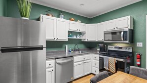 A modern kitchen with white cabinets, stainless steel appliances, and a wooden dining table. - Gemutliche Wohnung - hot tub, full kitchen, WiFi (Helen)