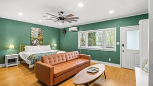 A bedroom with a bed, a brown leather sofa, a wooden coffee table, a ceiling fan, and a window with blinds. - Gemutliche Wohnung - hot tub, full kitchen, WiFi (Helen)