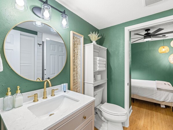 Une salle de bain avec un lavabo blanc, des robinets dorés, un miroir rond et des toilettes.