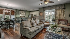 A spacious living room with a large gray sofa, a dining area with a wooden table and chairs, a kitchen with white cabinets, and a ceiling fan. - 4 Bedroom Vacation Home Walk to the Beach (North Myrtle Beach)