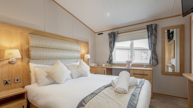 A hotel room with a large bed, wooden headboard, bedside tables, a desk, and a window with curtains. - Lodge No 44 | Stewart's Resort Cameron (Cameron)