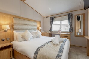A hotel room with a large bed, wooden headboard, bedside tables, a desk, and a window with curtains. - Lodge No 44 | Stewart's Resort Cameron (Cameron)