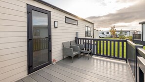 A covered outdoor deck with a sliding glass door, wicker furniture, and a view of neighboring RVs. - Lodge No 44 | Stewart's Resort Cameron (Cameron)