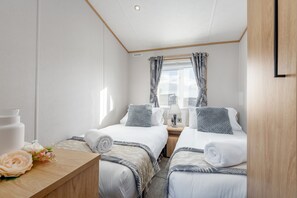 Et hotelværelse med to senge, et træskrivebord og et vindue med gardiner.