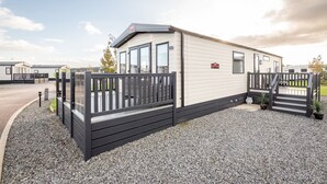 A mobile home with a fenced patio area, a gravel driveway, and a clear sky. - Lodge No 44 | Stewart's Resort Cameron (Cameron)