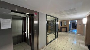 Un ascenseur avec un panneau indiquant qu'il est interdit de fumer, une porte en verre et un sol carrelé.