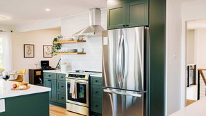 A modern kitchen with stainless steel appliances, green cabinetry, and a central island. - Stunning waterfront on bluff with sauna, firepit! (Weems)