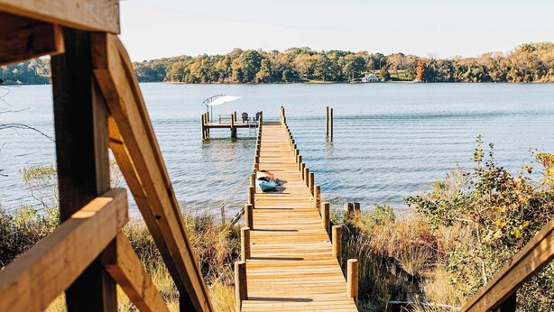 A wooden pier extending into a lake with boats docked at the end. - Stunning waterfront on bluff with sauna, firepit! (Weems)