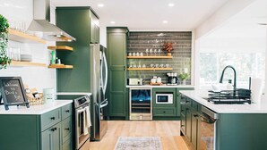 A modern kitchen with green cabinets, a built-in oven, a microwave, and a coffee maker. There is a rug on the floor and a sign that reads "Welcome to Birds Eye." - Stunning waterfront on bluff with sauna, firepit! (Weems)