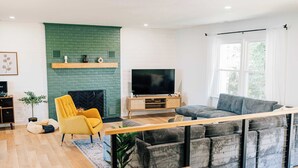 A modern living room with a green brick fireplace, a large flat-screen TV, a grey sectional sofa, and a yellow armchair. - Stunning waterfront on bluff with sauna, firepit! (Weems)