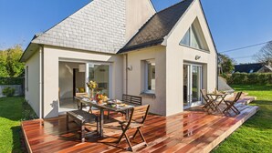 Ein modernes Haus mit einer Terrasse, einem Essbereich mit Gartenmöbeln und einem großen Fenster.