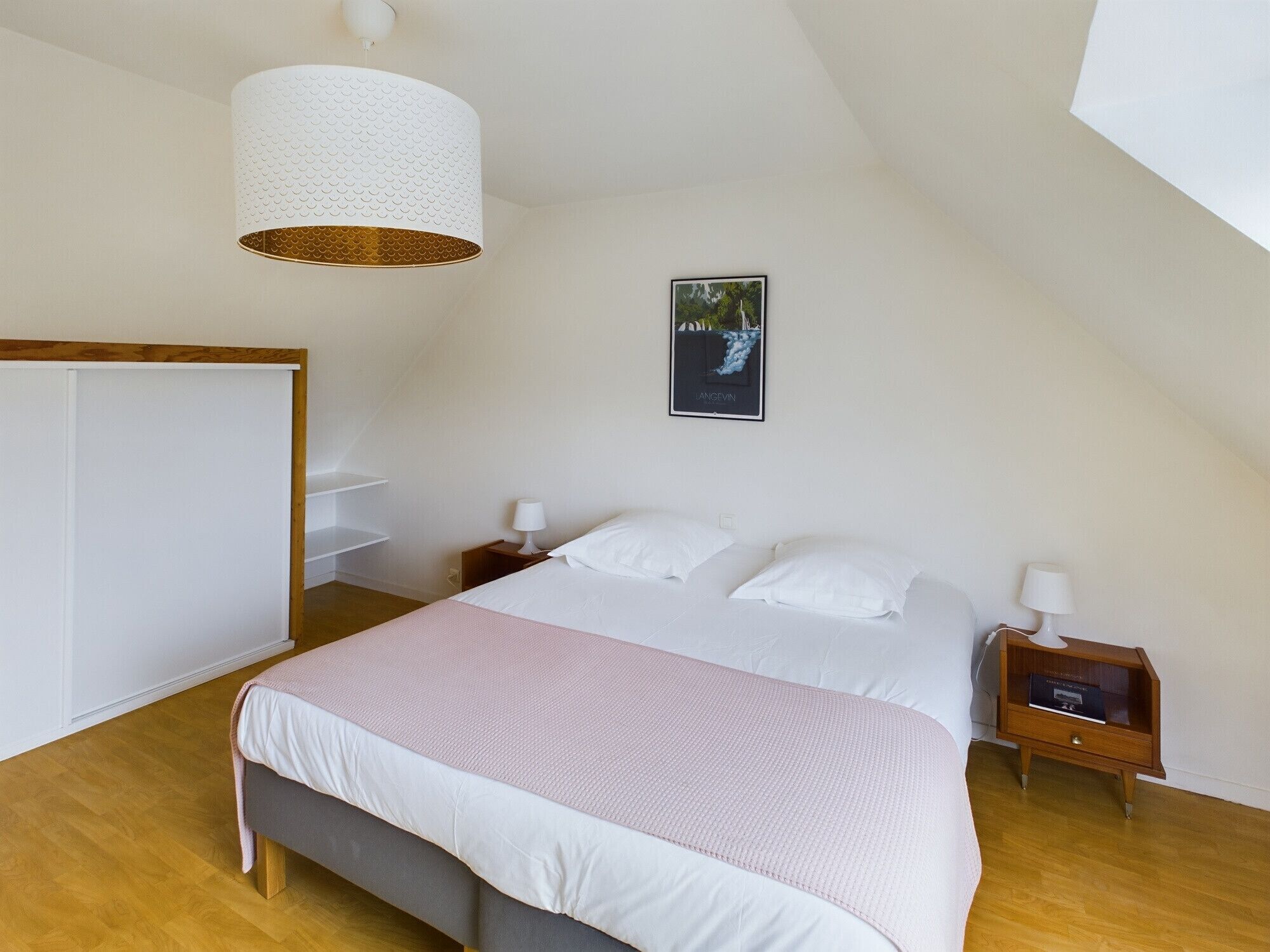 A bedroom with a bed, bedside tables, a hanging light fixture, and a framed picture on the wall.